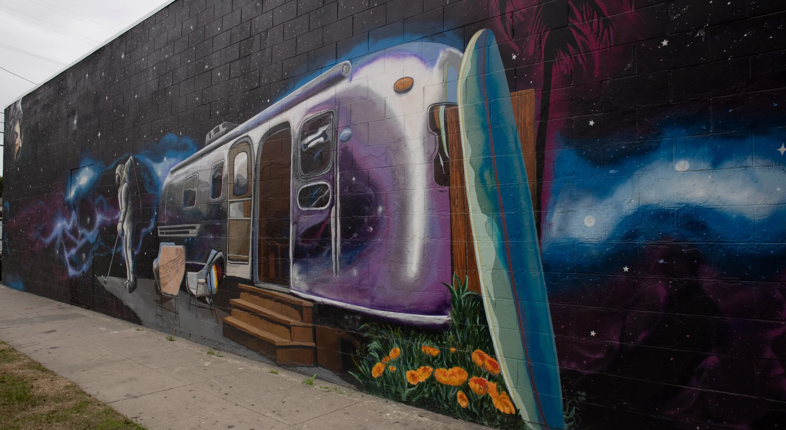 An Alleybrije mural of a vintage trailer under a starfield painted along a Long Beach alley wall